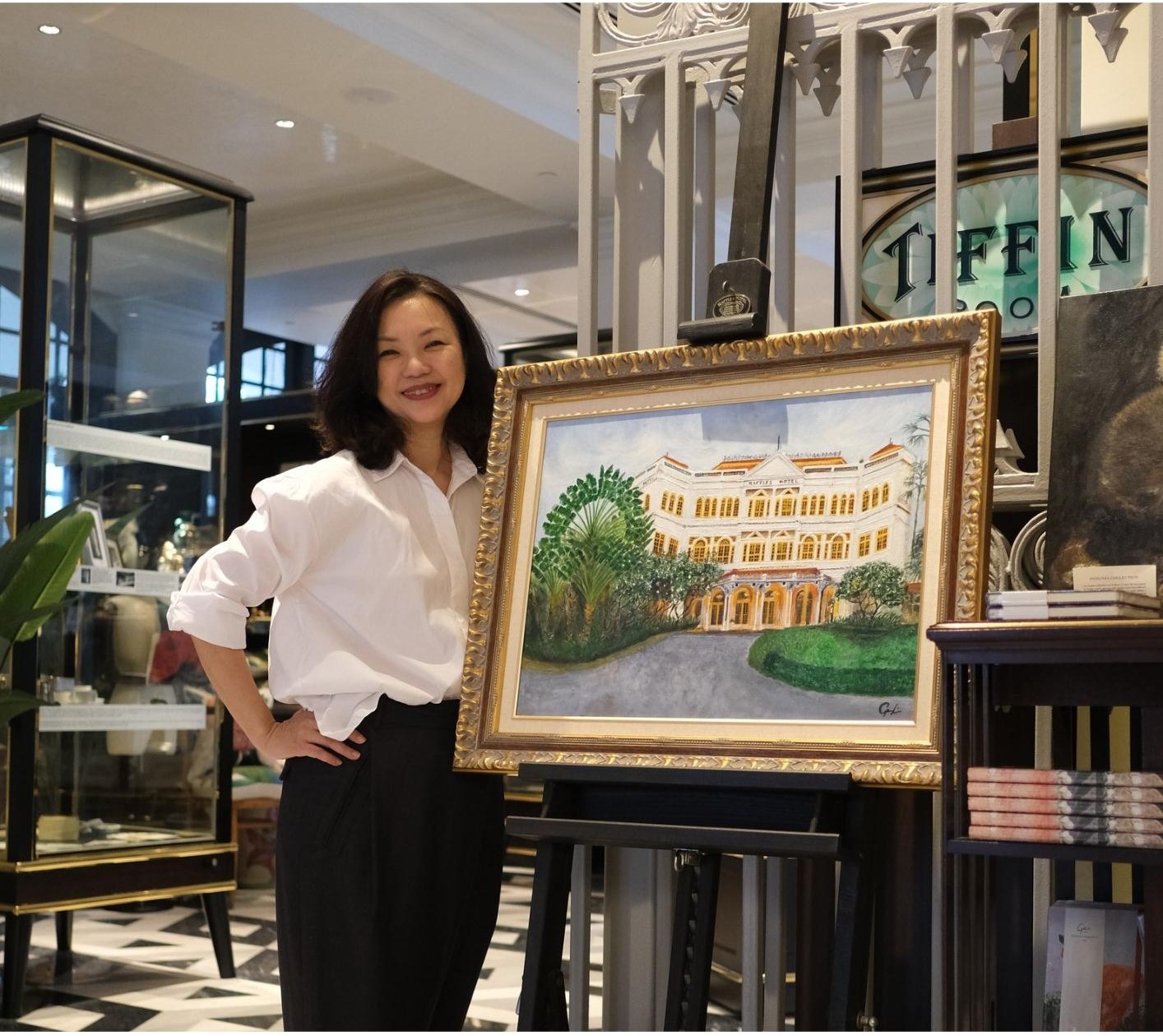 May Li Geoy, Managing Consultant of Vines Consulting, standing beside an oil painting of Raffles Hotel